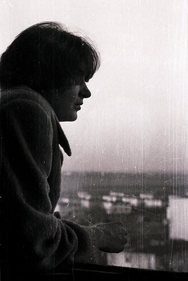 Black-and-white portrait of a person leaning on a window ledge, gazing outward. Mid-century hairstyle and clothing suggest 19...