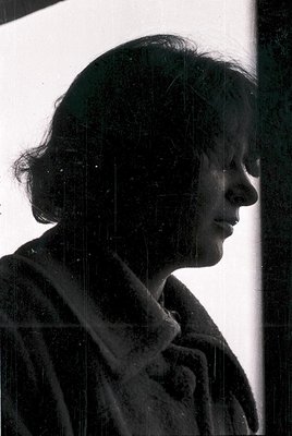 Silhouetted woman in a fur-trimmed coat, captured through rain-streaked glass. Mid-20th century fashion with short, layered h...