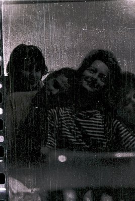 Vintage black-and-white photo of two women hugging through rain-streaked glass, likely taken indoors near a window. The woman...