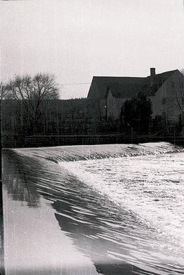 Black-and-white shot of a weir or spillway with cascading water in foreground, likely part of a dam or irrigation system. Mid...