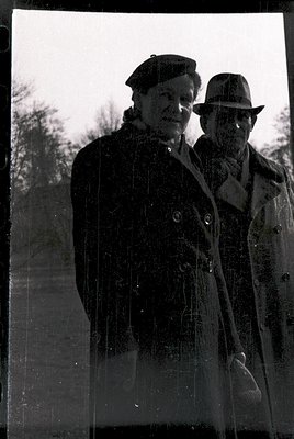 Vintage black-and-white portrait of two men in outdoor winter attire—one in a beret and trench coat, the other in a fedora an...