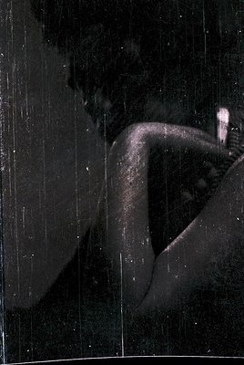 Black-and-white close-up of a seated figure in motion, captured through vertical rain or curtain-like fabric. The blurred sil...