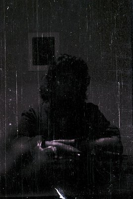 Silhouetted figure seated indoors, hands clasped, framed by vertical light streaks from a window. Vintage monochrome print wi...