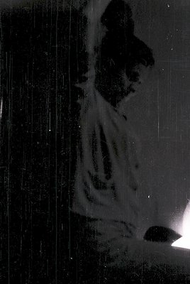 Silhouette of a person standing in heavy rain against a vertical surface, likely a window or glass door. The blurred motion s...