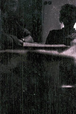 Black-and-white shot of a steamy shower scene, featuring two figures under cascading water. Reflections blur the glass, empha...