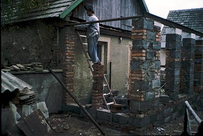 Man in 1970s-era workwear climbs ladder to repair weathered brick chimney stack, surrounded by scattered construction debris....