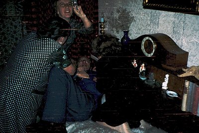 Vintage candid shot of a dimly lit interior with two women in 1970s-era clothing. One woman wears a polka-dot blouse and sung...