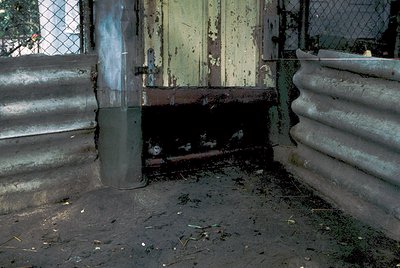 Abandoned concrete and metal structure with rusted, weathered surfaces. The corner of a building shows exposed rebar, peeling...