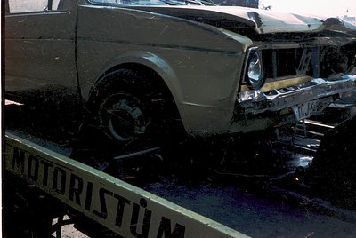 Severely damaged vintage truck on a flatbed tow truck labeled "Motoristüm," likely Turkish. Front end crushed, wheels exposed...