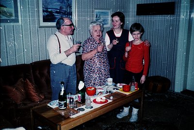 Family gathering in a dimly lit, retro interior with vertical blinds. Four adults/older adults pose with drinks, likely mid-1...