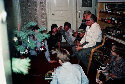 Family gathering in a mid-20th-century living room, likely 1970s–1980s. Decorated Christmas tree with ornaments and a star to...