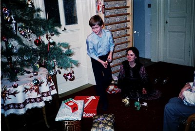 Vintage Christmas scene featuring a young boy in a light blue sweater holding a toy, standing beside a decorated pine tree ad...