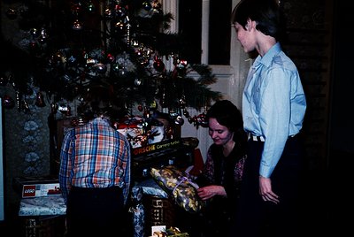 Vintage indoor holiday scene featuring three individuals decorating a Christmas tree with handmade ornaments and wrapped gift...