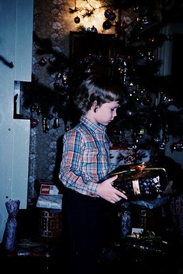 Vintage indoor scene featuring a child in a plaid shirt examining a wrapped gift under a festive tree adorned with ornaments ...