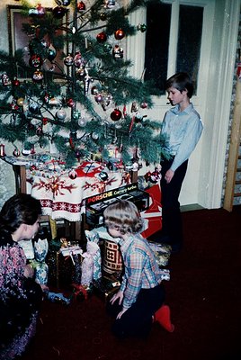 Vintage 1970s holiday scene featuring a decorated Christmas tree adorned with glass ornaments, red baubles, and tinsel. Three...