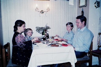 Family dinner scene in a vintage-style dining room, 1970s. Four adults seated around a table with a floral centerpiece, wine ...