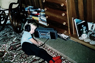 Vintage indoor scene: child in 1970s-era striped shirt and red socks sits cross-legged on patterned carpet, engrossed in a po...