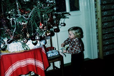 Vintage Christmas scene featuring a child in plaid shirt examining wrapped gifts under a decorated pine tree adorned with orn...