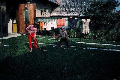 Two boys play croquet in a residential backyard, 1960s-1970s. Wooden house with numbered door (609), hanging laundry, and a w...