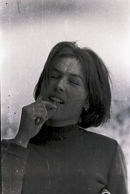 Vintage black-and-white portrait of a woman mid-laughter, hand raised to mouth. She wears a choker necklace and short, layere...