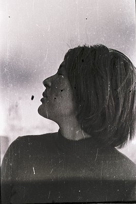 Vintage black-and-white portrait of a woman with short, layered hair, shot in profile. The grainy texture and lighting sugges...