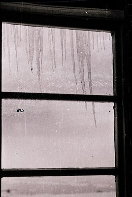 Close-up of rain streaks on a double-pane window, likely residential or small office. Vertical lines from dripping water crea...