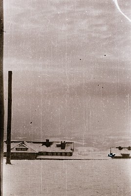 Aerial view of a single-story industrial building with a flat roof, likely a warehouse or factory, situated near a waterfront...