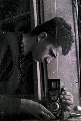 Vintage black-and-white portrait of a man examining a **Zeiss Ikon Contax II** twin-lens reflex camera, likely mid-20th centu...