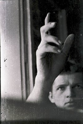 Vintage black-and-white portrait showing a hand raised in a peace sign against a frosted window, with a partial face visible ...
