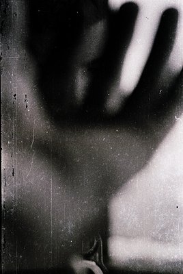 Vintage black-and-white close-up of a hand resting on a textured, slightly scratched surface. The hand’s fingers are slightly...