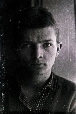 Vintage black-and-white portrait of a young man in a patterned sweater, likely mid-20th century. Direct gaze with neutral exp...