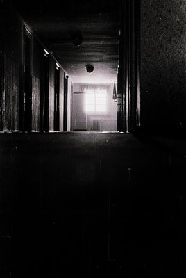 Low-angle shot of a dimly lit hallway with exposed wooden beams, suggesting mid-20th century industrial or institutional arch...
