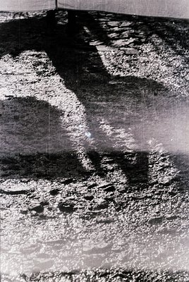 Vintage black-and-white photo of a **reflective water surface** with faint, abstract **boat footprints** and **ripples**. Com...