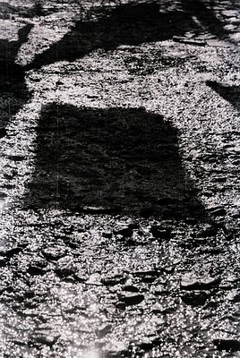 Close-up of a square-shaped, sunken concrete patch on a cracked asphalt surface, likely from road resurfacing or utility work...