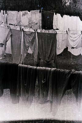 Black-and-white photograph of laundry drying on a clothesline by a waterfall, likely mid-20th century. Sheets, towels, and ga...