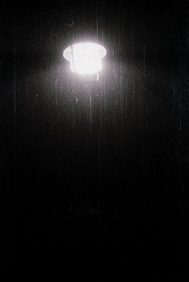 Classic streetlamp bathed in rain, casting a bright circular glow against a dark night sky. The spherical bulb and classic de...