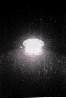 Vintage close-up of a square, frosted glass lightbulb with a metal base, illuminated against a dark, textured background. Lik...