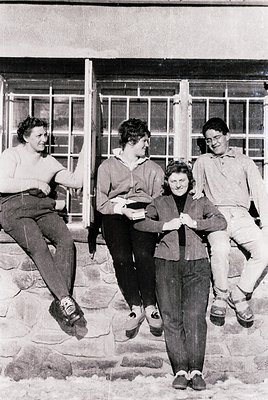 Four individuals pose casually on stone steps in 1960s-70s outdoor setting. Women wear knee-length sweaters, trousers, and sn...