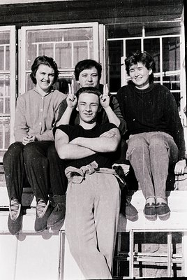 Four individuals pose casually on a window ledge, likely mid-20th century (1950s–1960s). Short haircuts, simple clothing (blo...