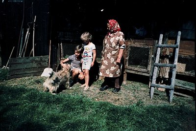 Vintage rural scene featuring a woman in floral dress and headscarf petting a dog with two children in 1970s-era clothing. Wo...