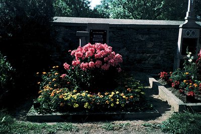 Vibrant floral tribute atop a stone mausoleum with classical architectural details. Lush pink roses dominate the center, surr...