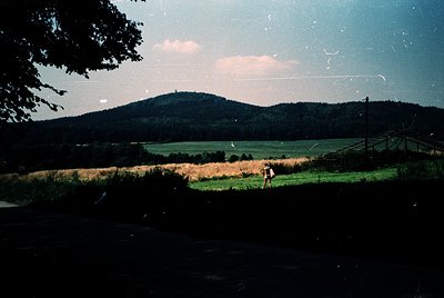Vintage landscape shot featuring a lone figure walking through a golden field under a hazy sky. Rolling hills and a distant m...