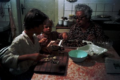 Vintage kitchen scene featuring a woman and two children preparing food on a wooden cutting board. White-tiled walls and retr...