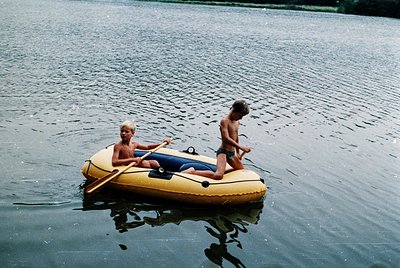 Two individuals in a yellow inflatable raft on calm waters, likely a lake or river. The older person rows while the younger s...