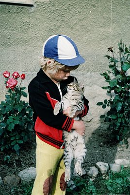 A child in vintage 1970s-style clothing—yellow pants with red patches, a red-and-black striped sweater, and a blue-and-white ...