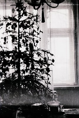 Vintage black-and-white interior featuring a modestly decorated Christmas tree with sparse ornaments and a single candle-like...