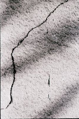 Close-up of weathered plaster wall showing deep cracks and peeling texture, likely from structural settling or age. The verti...