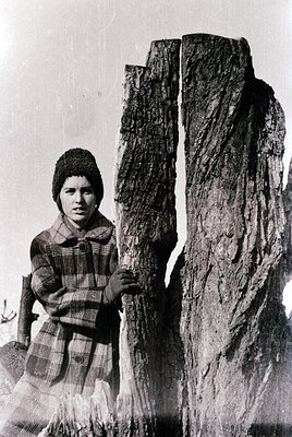 Black-and-white portrait of a young girl in traditional alpine attire—plaid skirt, checkered sweater, and knitted cap—posing ...