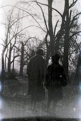 Vintage sepia-toned photograph of two figures walking away from the camera through a leafless forest path, likely late 19th t...