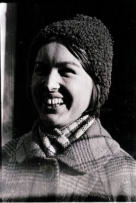 Black-and-white portrait of a person wearing a knitted headscarf and a patterned scarf, likely from the 1950s–1970s. Warm, ca...